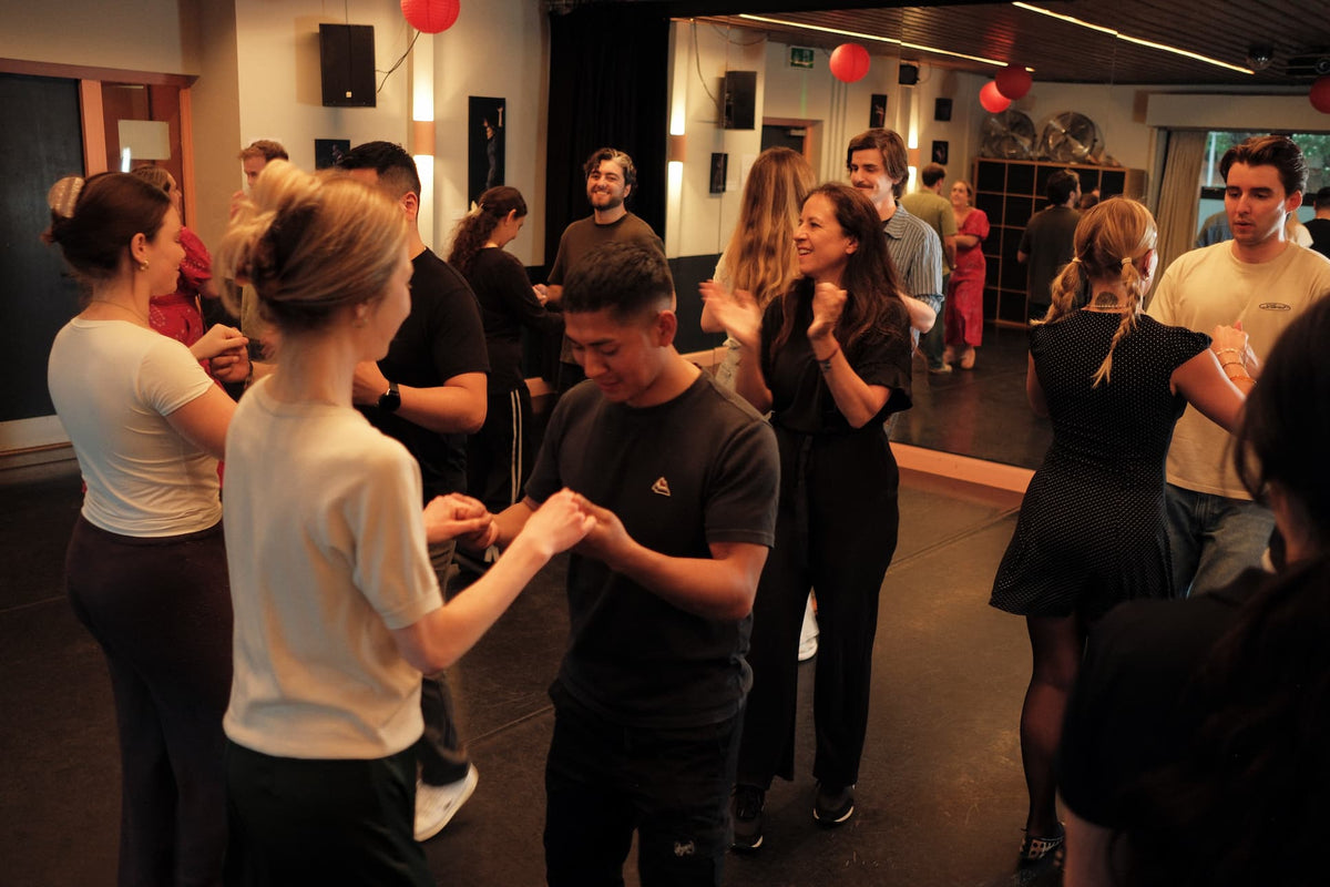 A group of people dancing in a dimly lit indoor studio or event space with red balloons hanging from the ceiling.